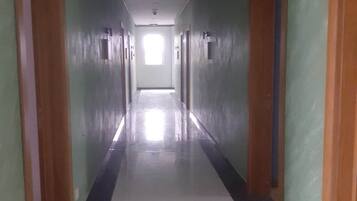 Un pasillo largo y estrecho con puertas a ambos lados, que conduce a una habitación luminosa al final.