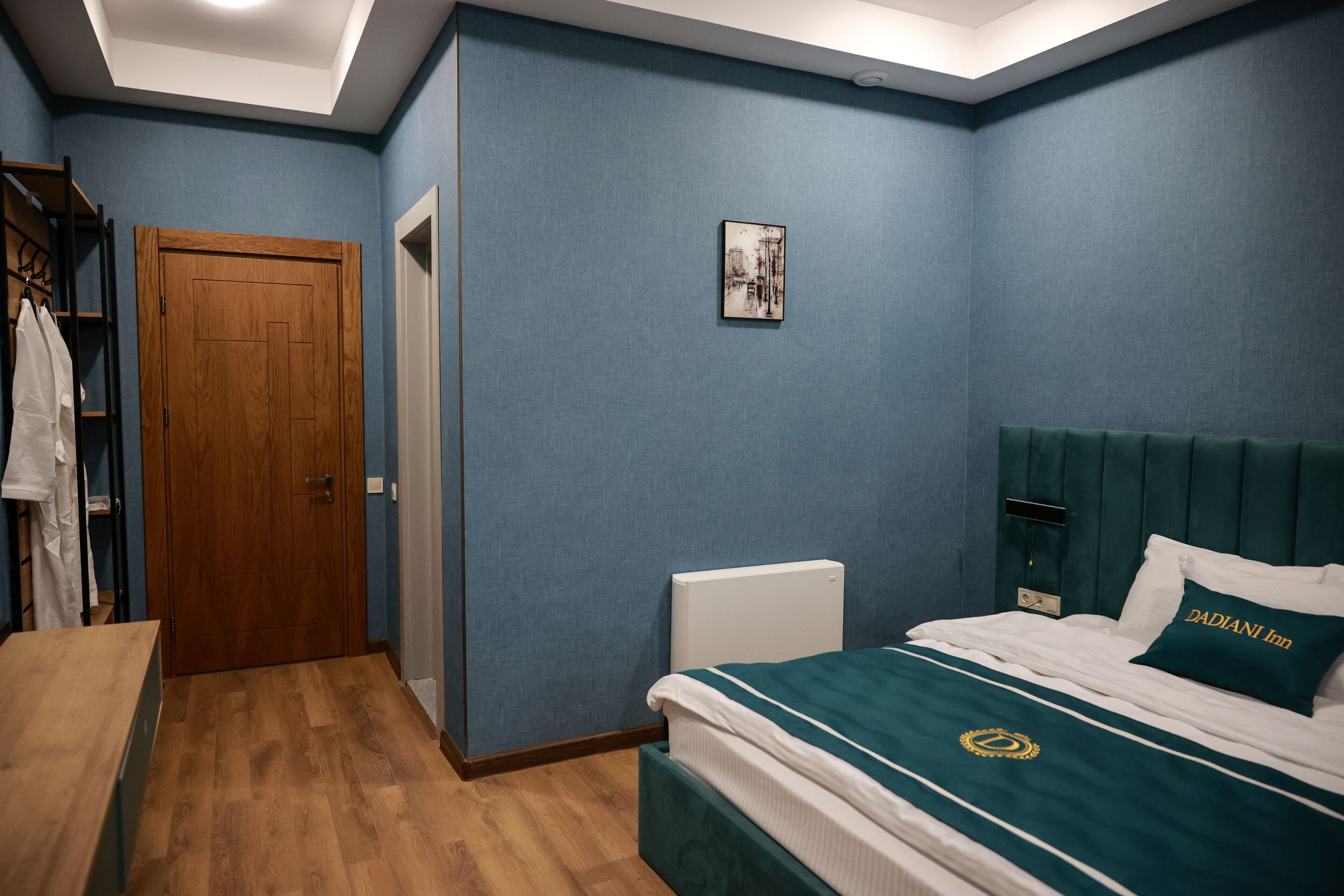 A bedroom with a wooden door, a radiator, a bed with a green headboard, and a wall-mounted artwork.