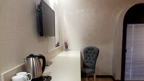 A modern room with a white counter, a black chair, a small table with a kettle and cups, and a TV mounted on the wall. - DADIANI Inn (Zugdidi)