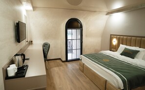 A hotel room with a bed, a chair, a desk with a kettle, and a television on the wall.