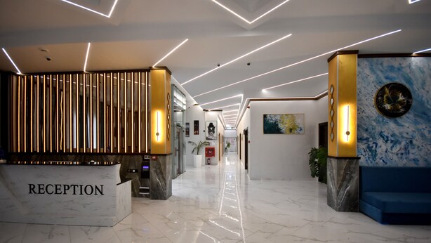 A modern reception area with a marble floor, a reception desk labeled "RECEPTION," and a blue seating area. - DADIANI Inn (Zugdidi)