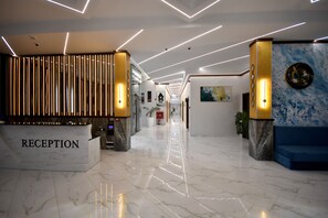 Un área de recepción moderna con suelo de mármol, un mostrador de recepción que indica "RECEPTION" y una zona de estar azul.