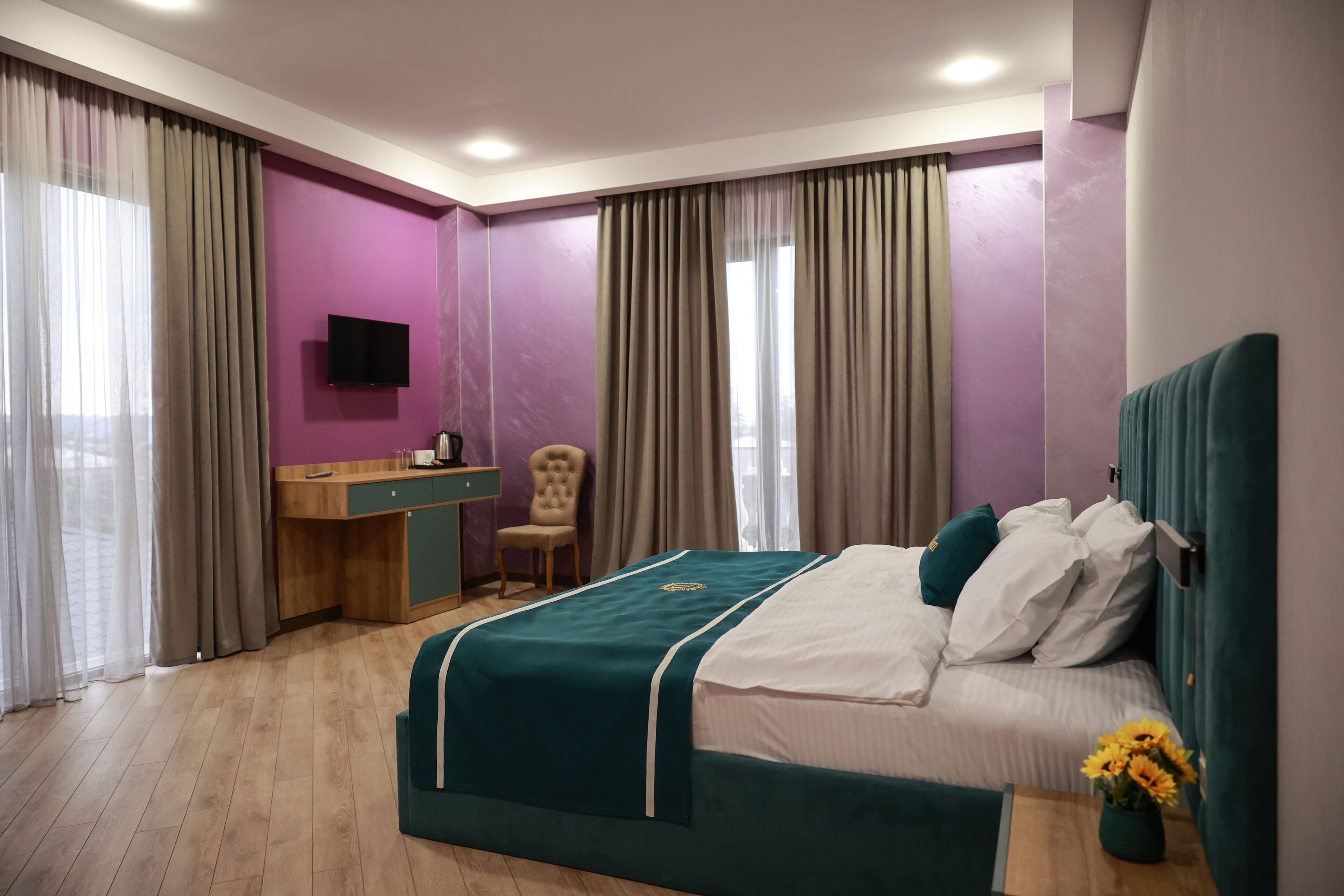 A hotel room with a bed, a desk, a chair, a TV, and a window with curtains.