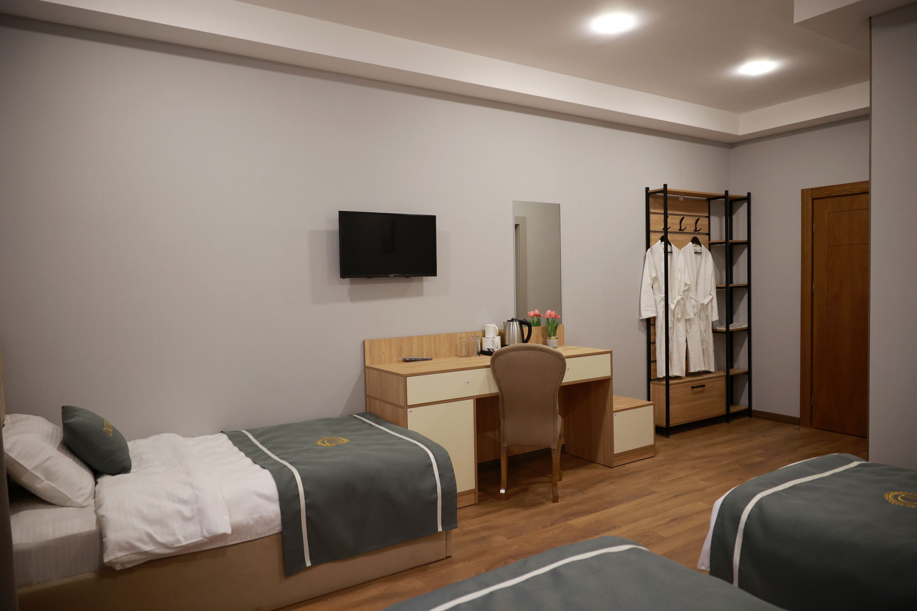 A hotel room with two single beds, a desk, a chair, a TV, a wardrobe, and a mirror.