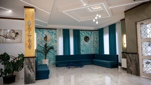 A modern lobby with a marble floor, blue seating area, and a large potted plant. - DADIANI Inn (Zugdidi)