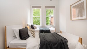 A bedroom with two beds, white walls, and large windows with a view of greenery. - Pet Friendly - Character and Charm on Emerald Hill (South Melbourne)