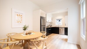 A modern kitchen with a refrigerator, stove, and dishwasher. There is a dining area with a wooden table and chairs. - Pet Friendly - Character and Charm on Emerald Hill (South Melbourne)