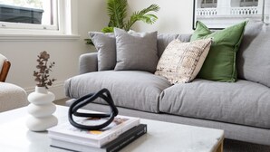 A grey sofa with multiple cushions, a white vase with dried flowers, and a stack of books on a white coffee table. - Pet Friendly - Character and Charm on Emerald Hill (South Melbourne)