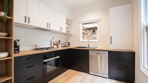 A modern kitchen with black and white cabinetry, a built-in oven, and a dishwasher. - Pet Friendly - Character and Charm on Emerald Hill (South Melbourne)