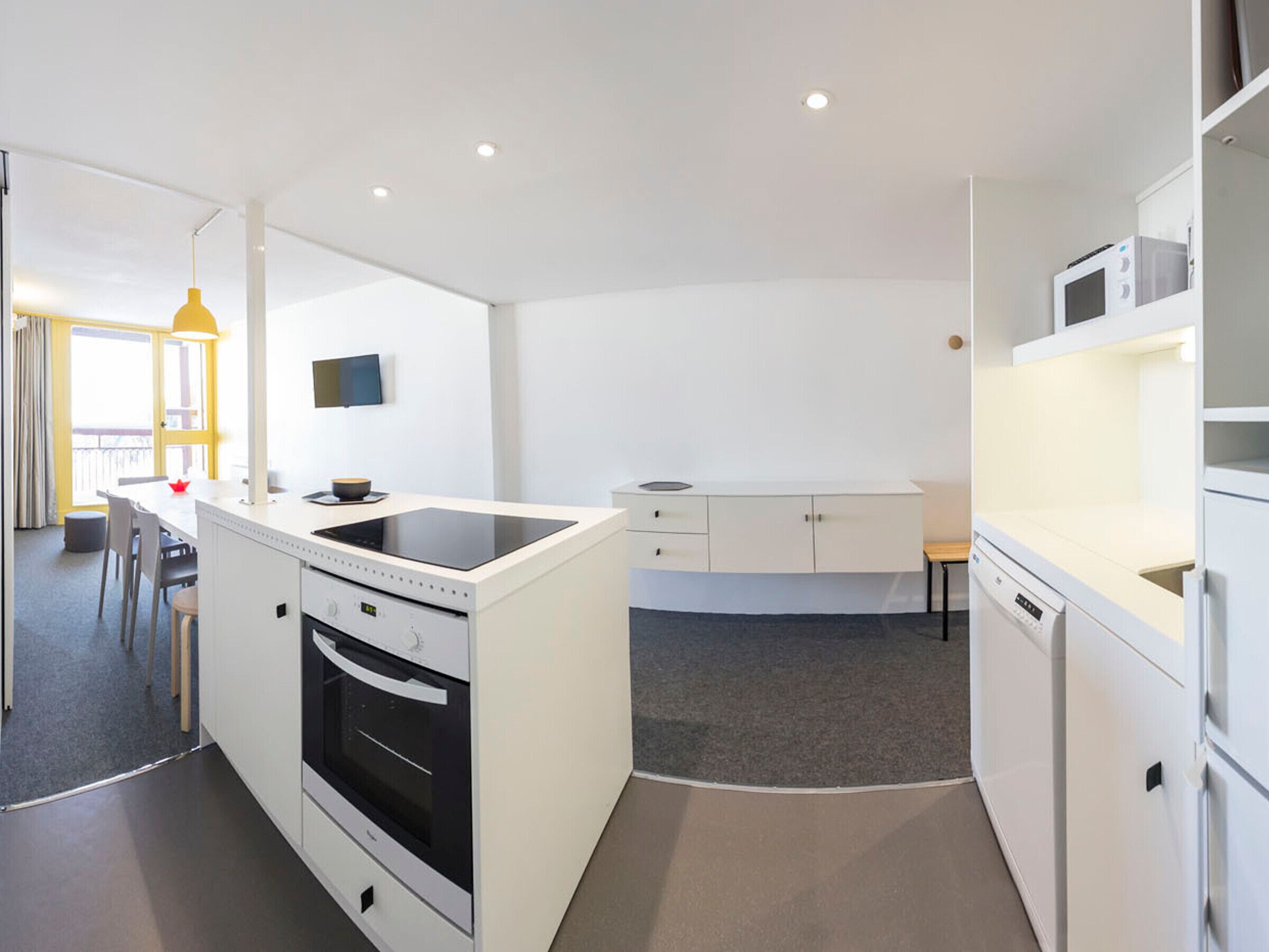 Una cocina moderna con armarios blancos, horno integrado, microondas y comedor con mesa y sillas.