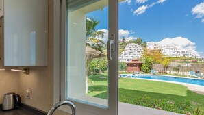 Cocina moderna con un amplio ventanal que da a una piscina y edificios blancos.