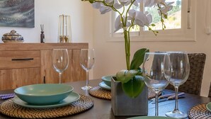 Una mesa de comedor con cuencos verdes, copas de vino y un florero con flores blancas.