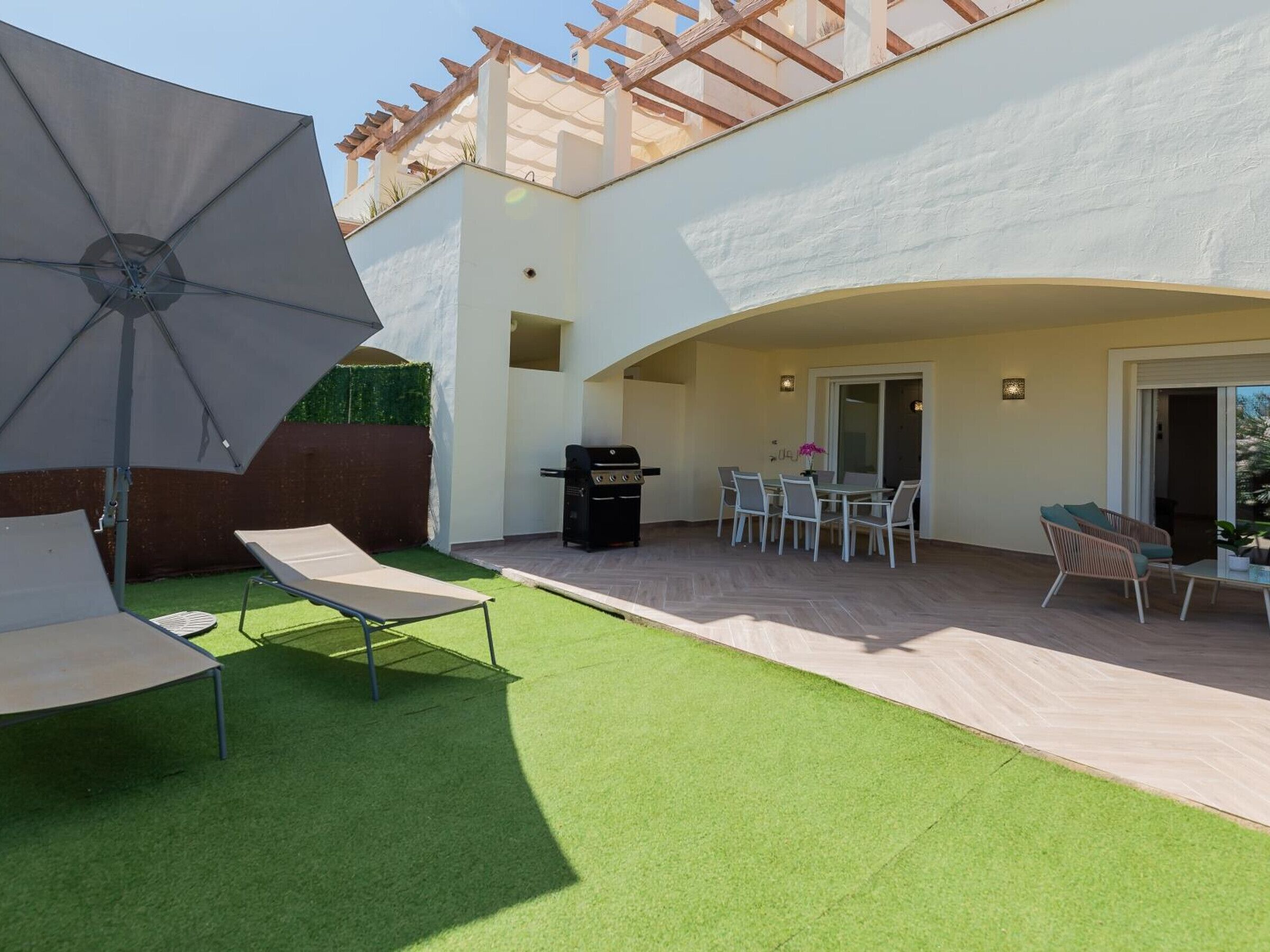 Un patio con una parrilla, mobiliario exterior y una pérgola.