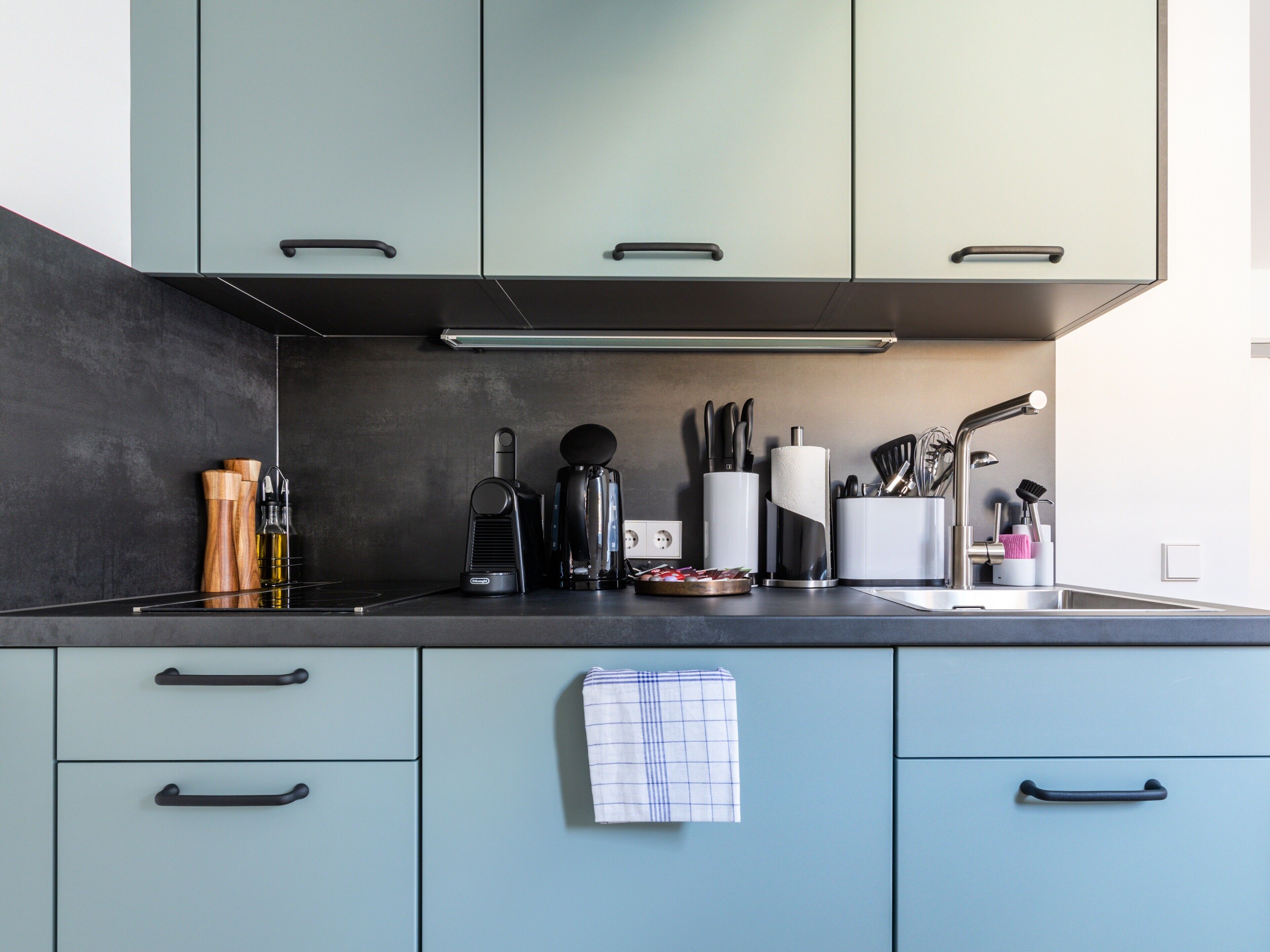 A modern kitchen with light blue cabinets, a black countertop, and various kitchen appliances and utensils.