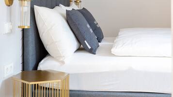 A modern bedroom with a grey headboard, white and dark grey pillows, a bedside table, and a wall-mounted light fixture.