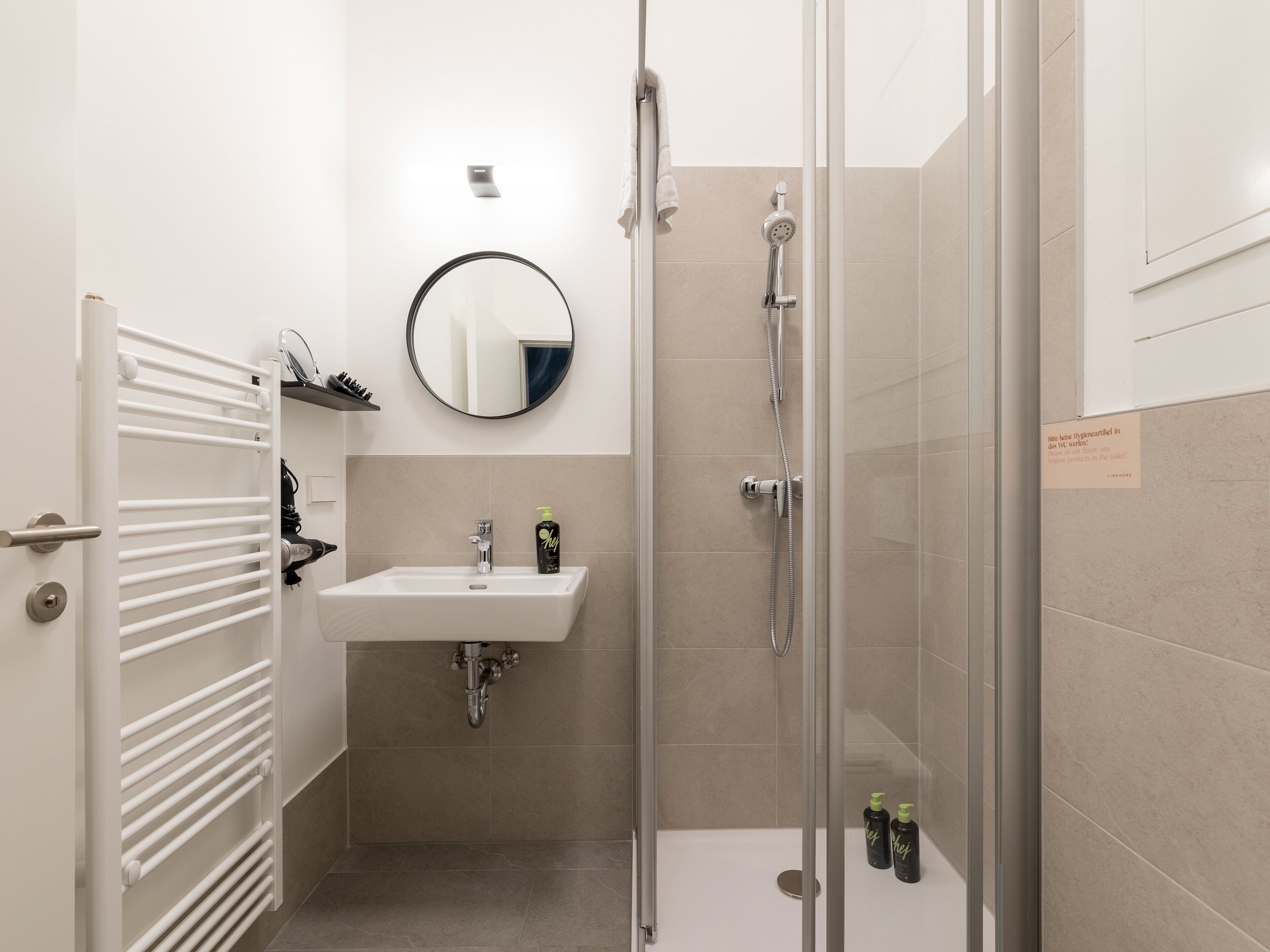 A modern bathroom with a glass shower enclosure, a sink with a mirror above it, and a towel rack.