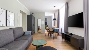 Un salon moderne avec un canapé gris, une table basse ronde, un coin repas avec une table et des chaises, un téléviseur fixé au mur et une armoire.
