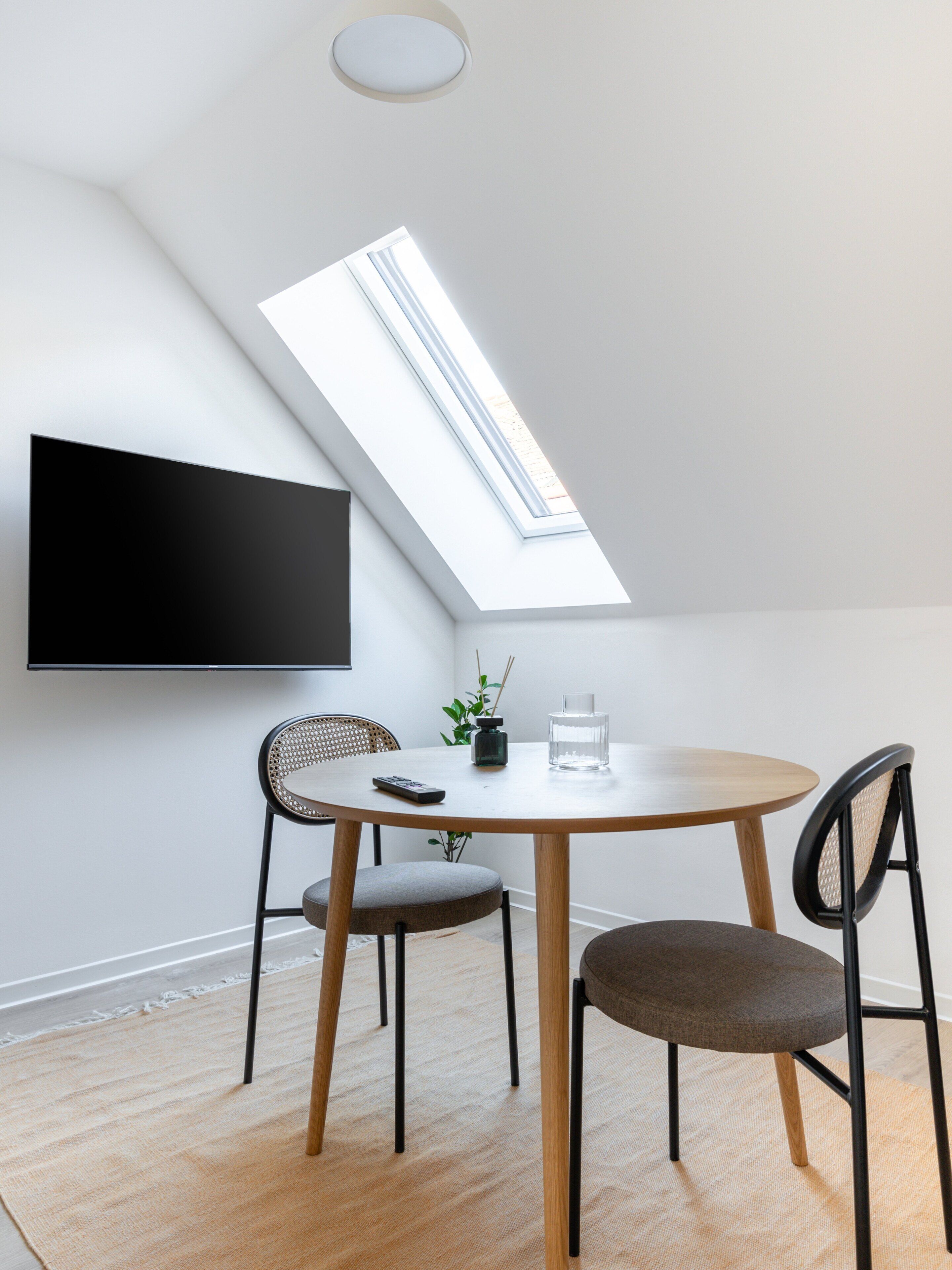 A modern dining area with a skylight, a flat-screen TV, and two chairs.