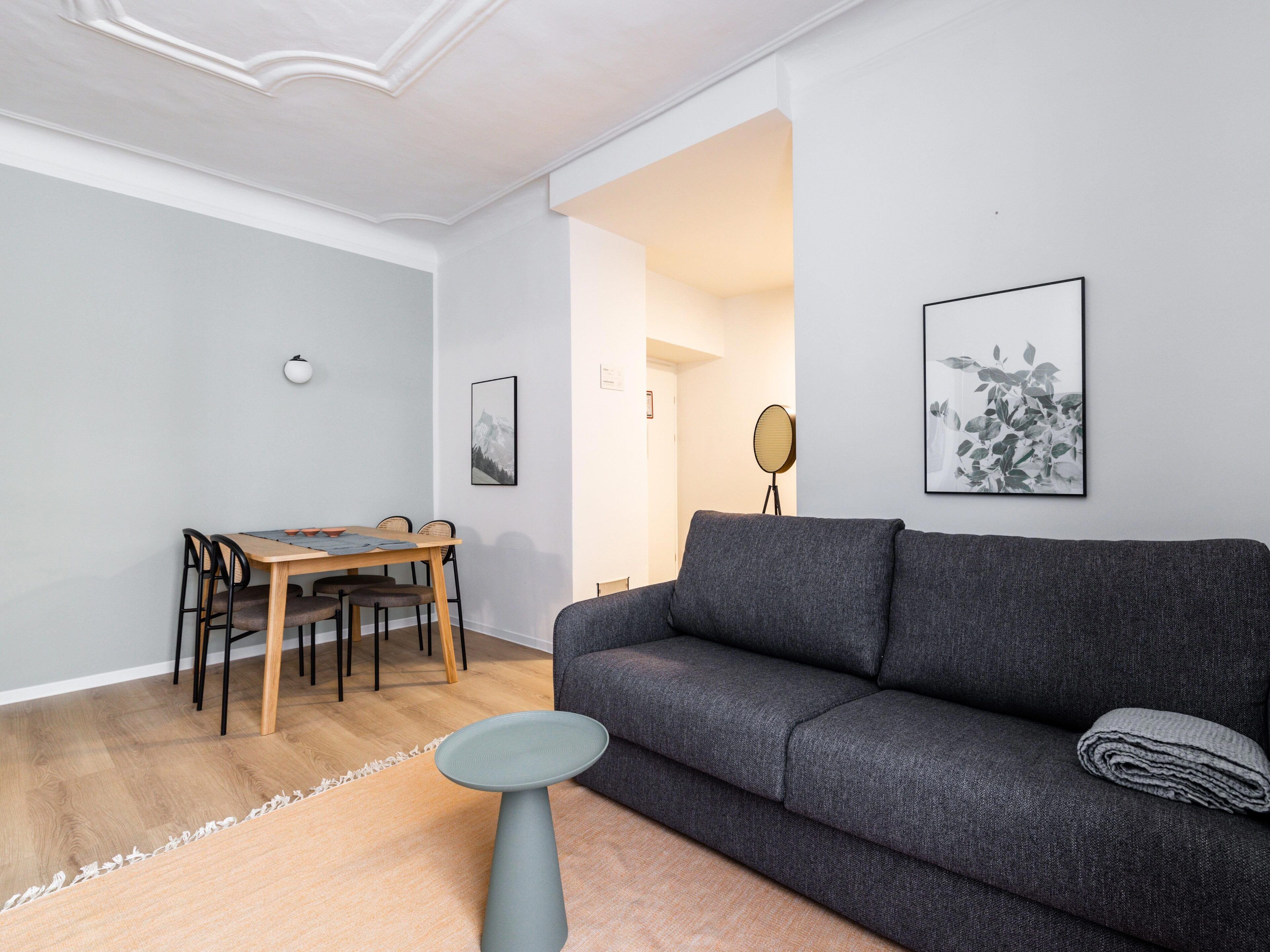 Un salon moderne avec un canapé gris, une table à manger en bois avec des chaises et une petite table ronde.