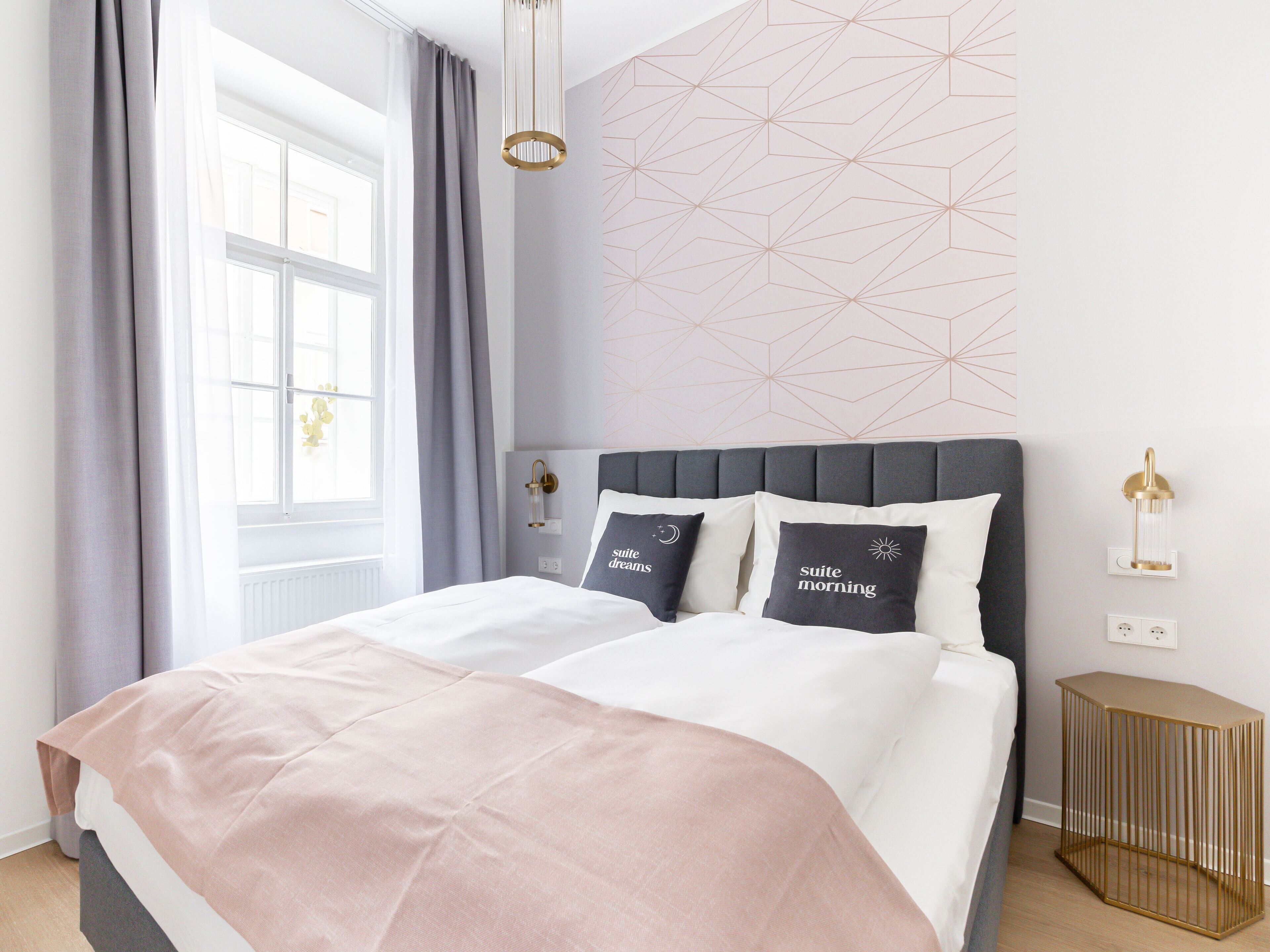 Quarto moderno com uma cama grande, cortinas cinzas, design geométrico na parede e um abajur.