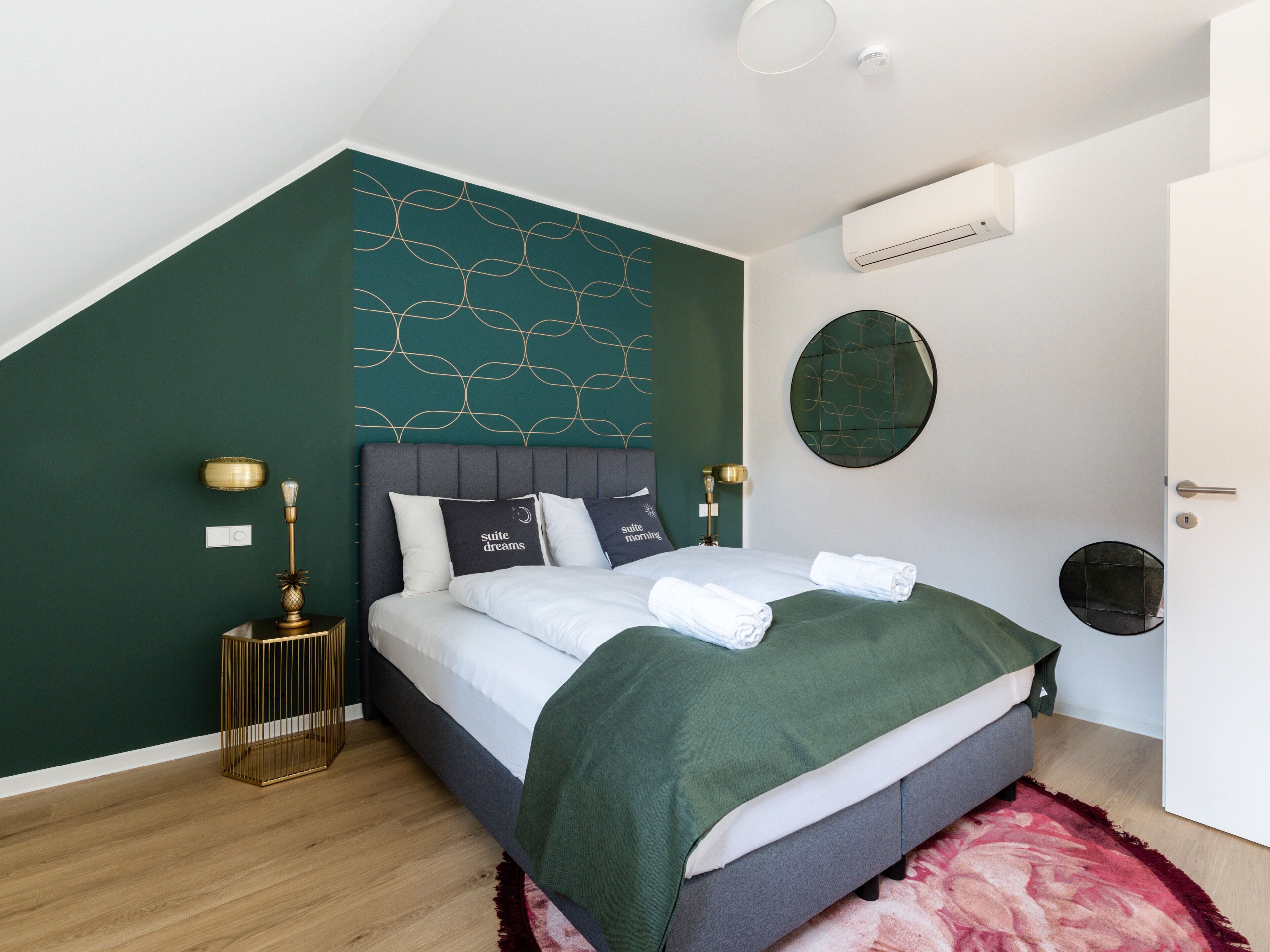 A modern bedroom with a bed, green walls, and a decorative wall panel.