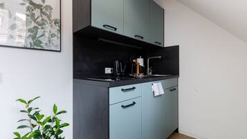 A modern kitchen with teal cabinets, black countertops, and a stainless steel range hood.