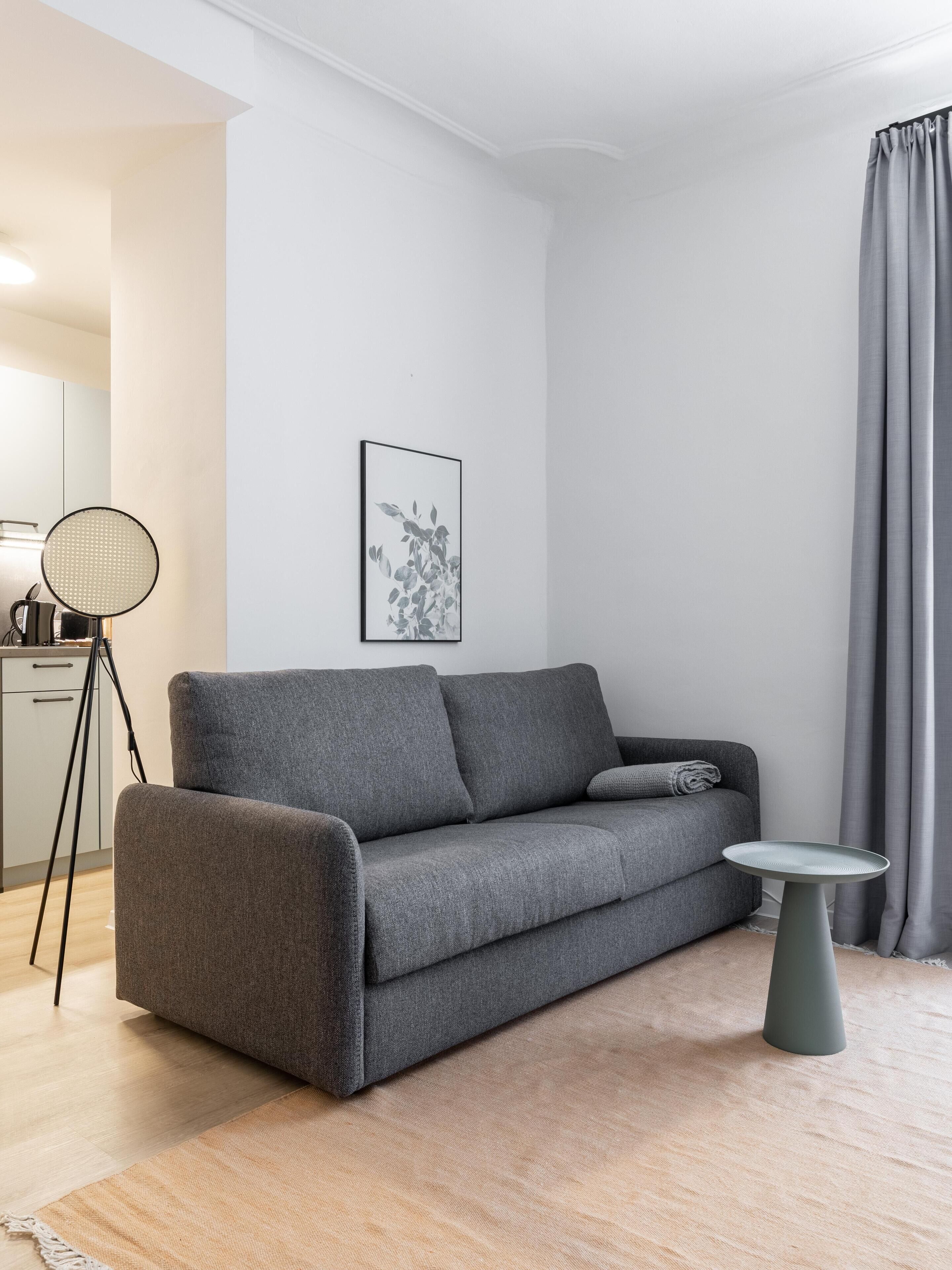 Een moderne woonkamer met een grijze bank, een kleine ronde tafel en een vloerlamp.