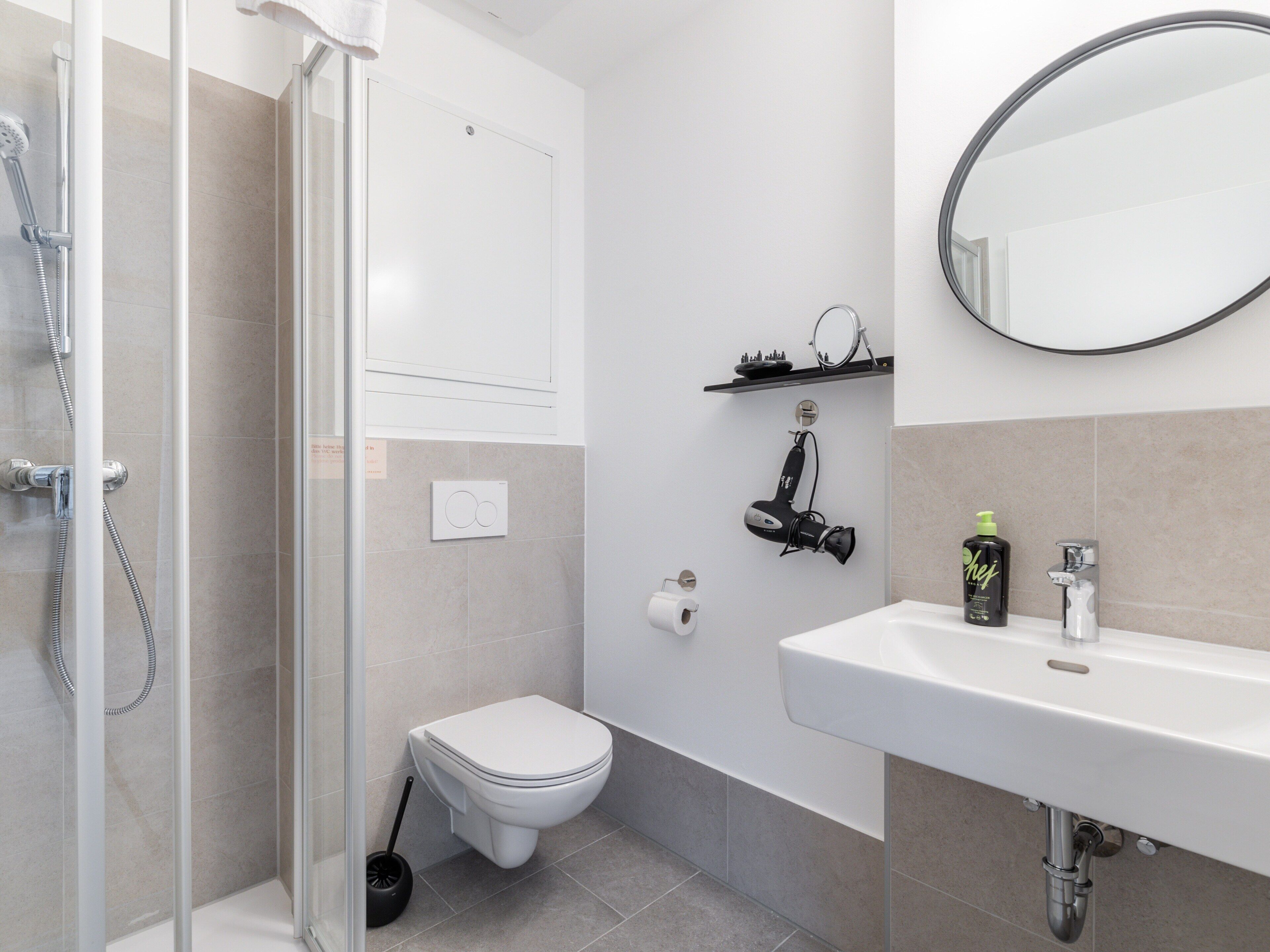 A modern bathroom with a shower, toilet, sink, and a mirror.