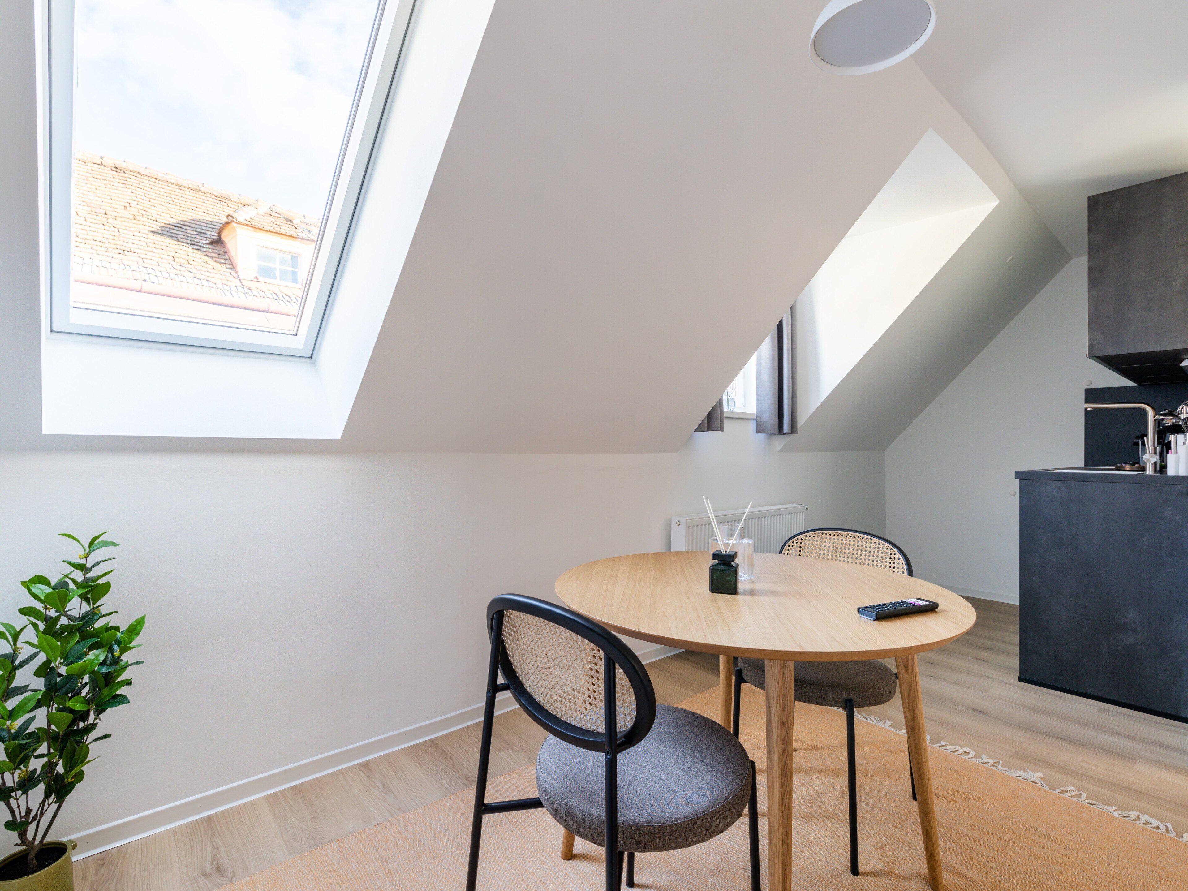 A modern kitchen with a dark countertop, a round dining table with chairs, and a skylight.