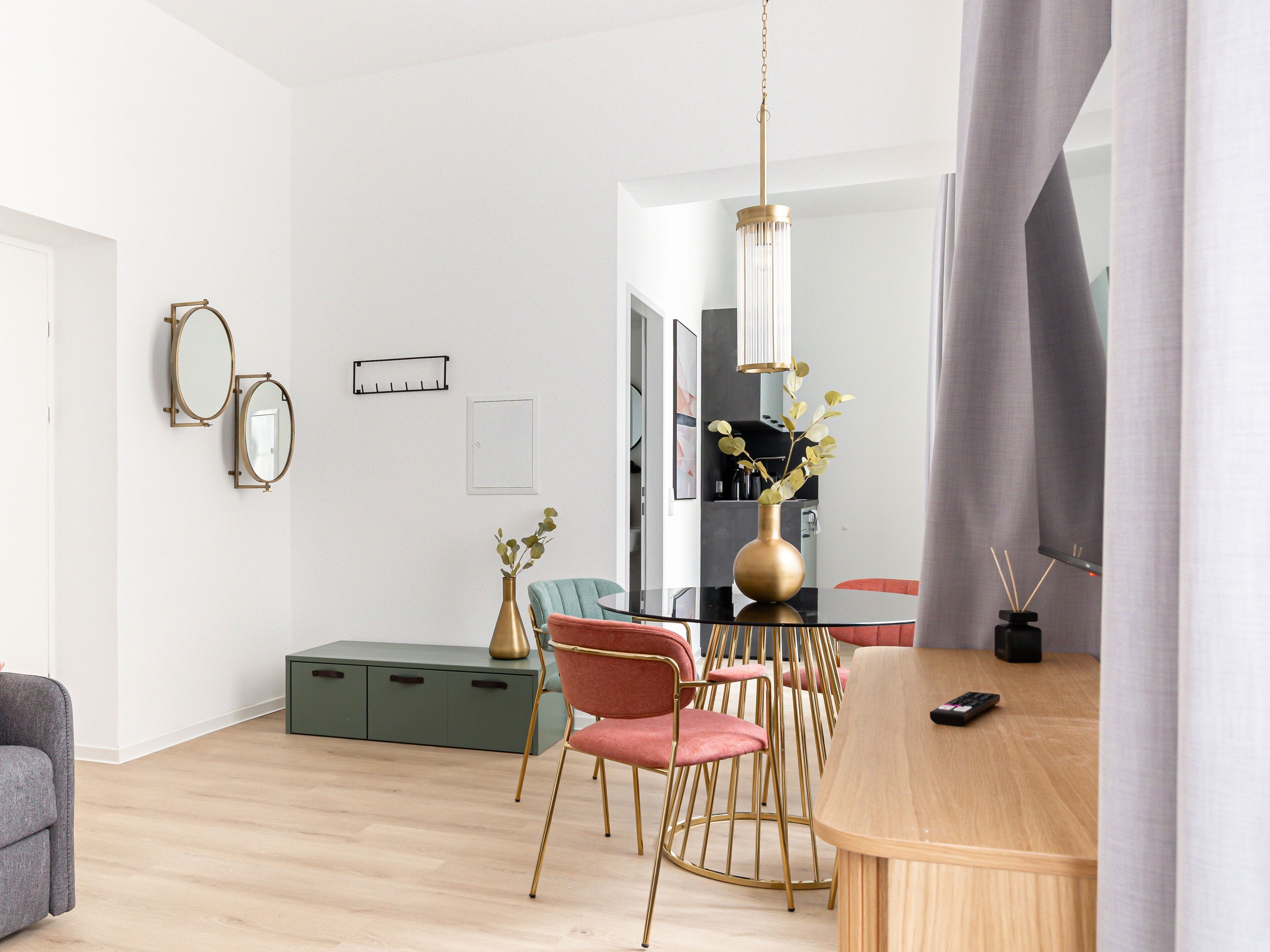 A modern dining area with a wooden table, gold chairs, and a vase with greenery.