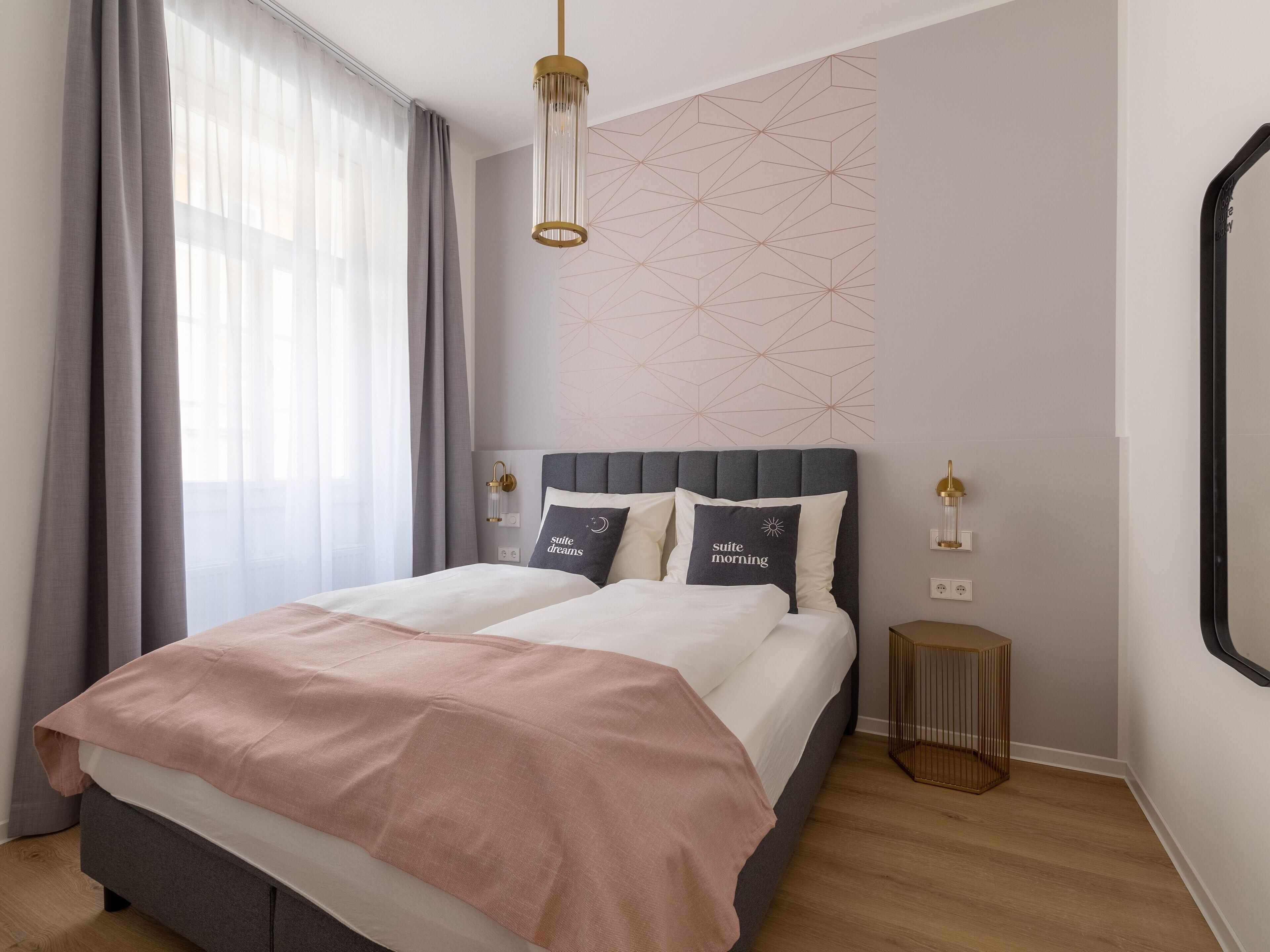 A modern bedroom with a bed, bedside lamps, and a geometric wall design.