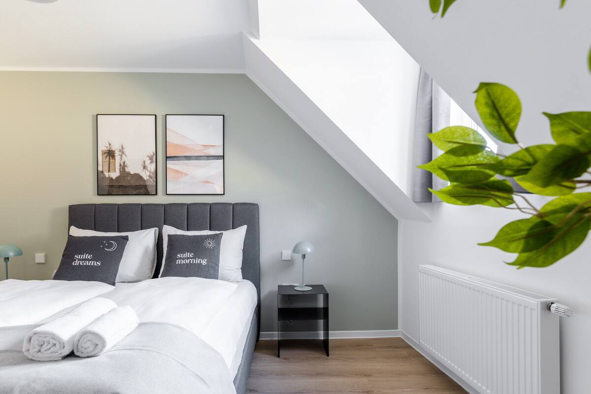 Um quarto moderno com uma cama, mesas de cabeceira, um radiador e uma janela com uma planta.