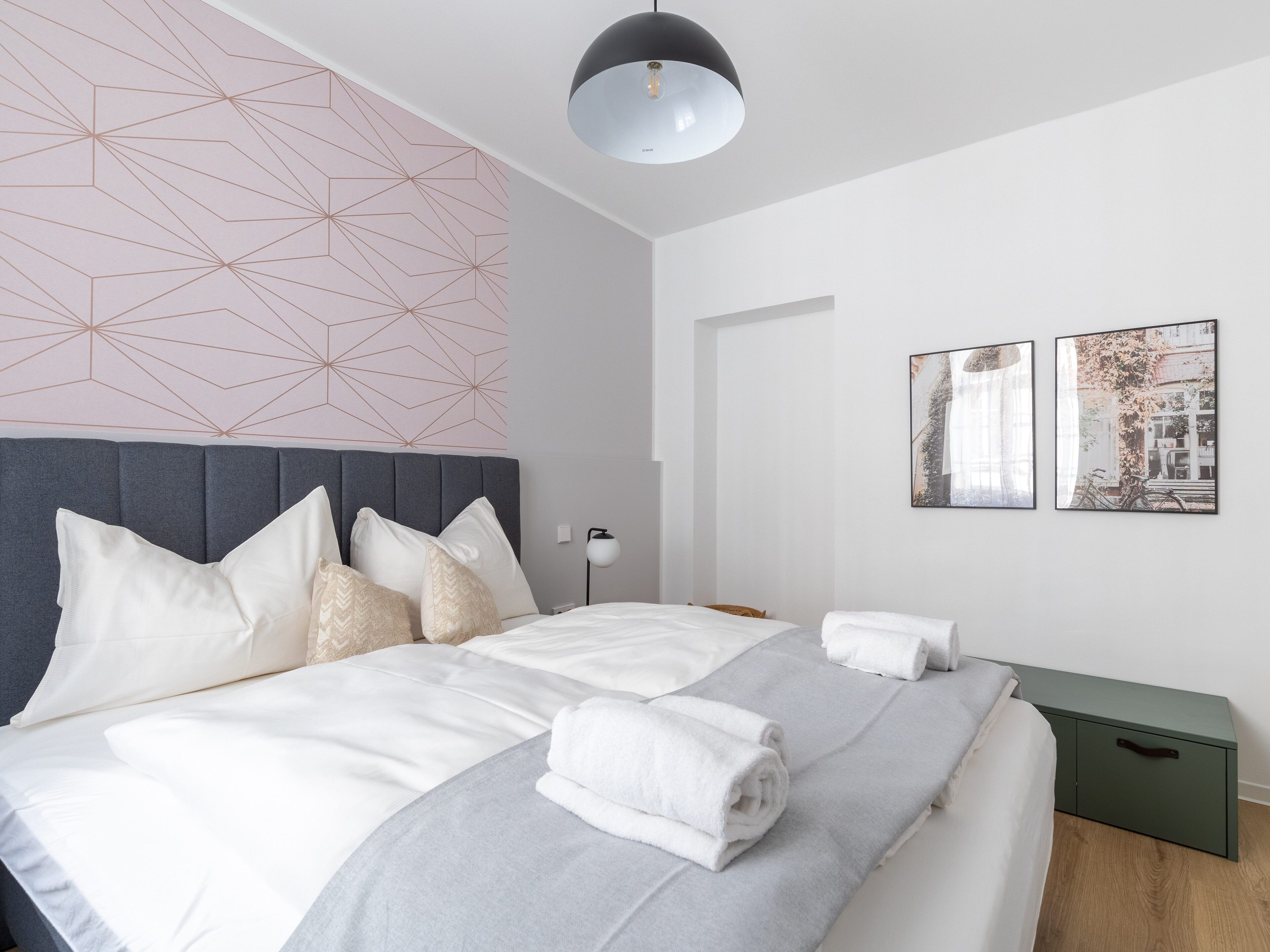 Ein modernes Schlafzimmer mit grauem Kopfteil, weißer Bettwäsche und einer Wand mit geometrischem Muster.