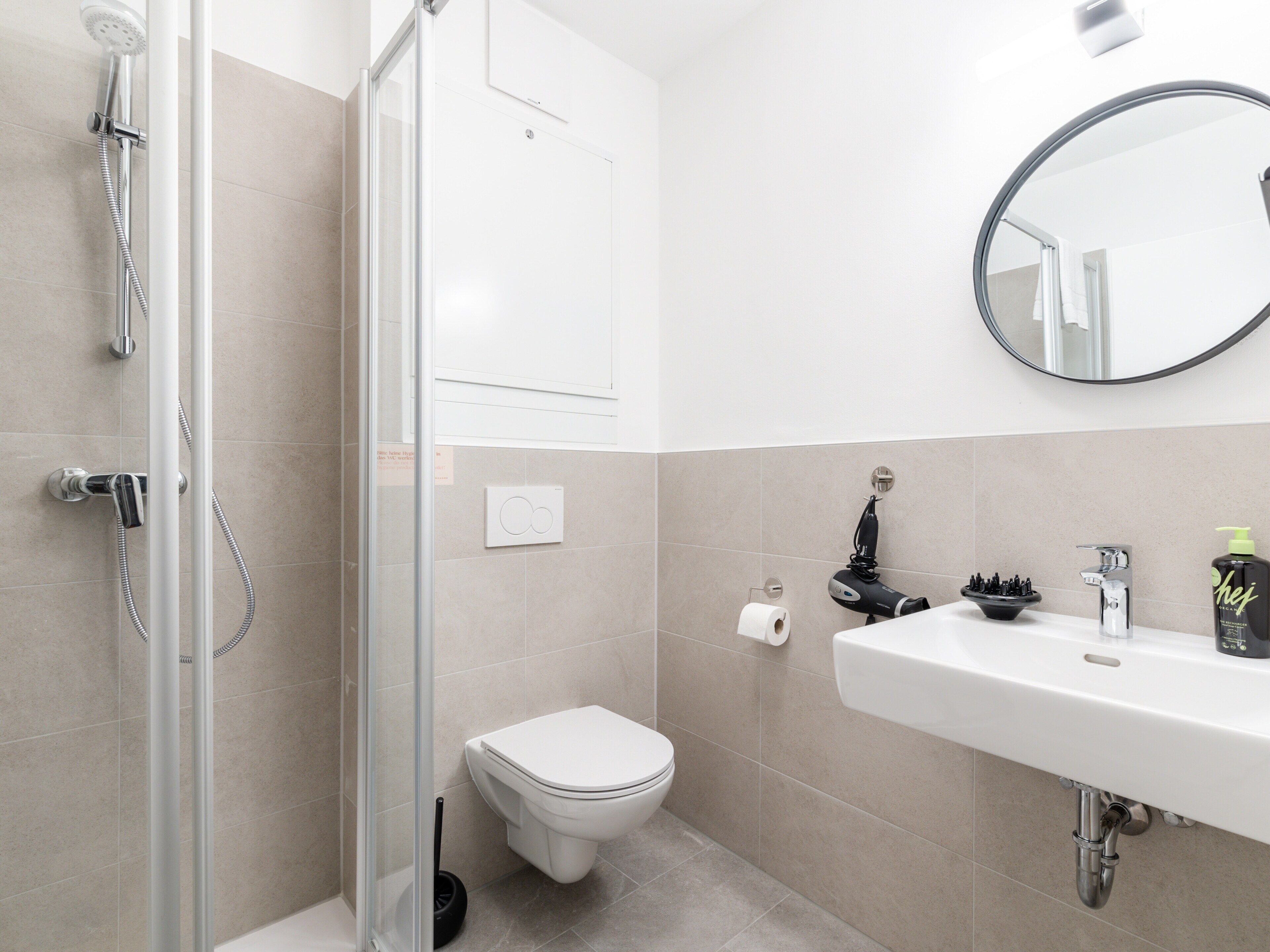 A modern bathroom with a shower, toilet, sink, and a mirror.
