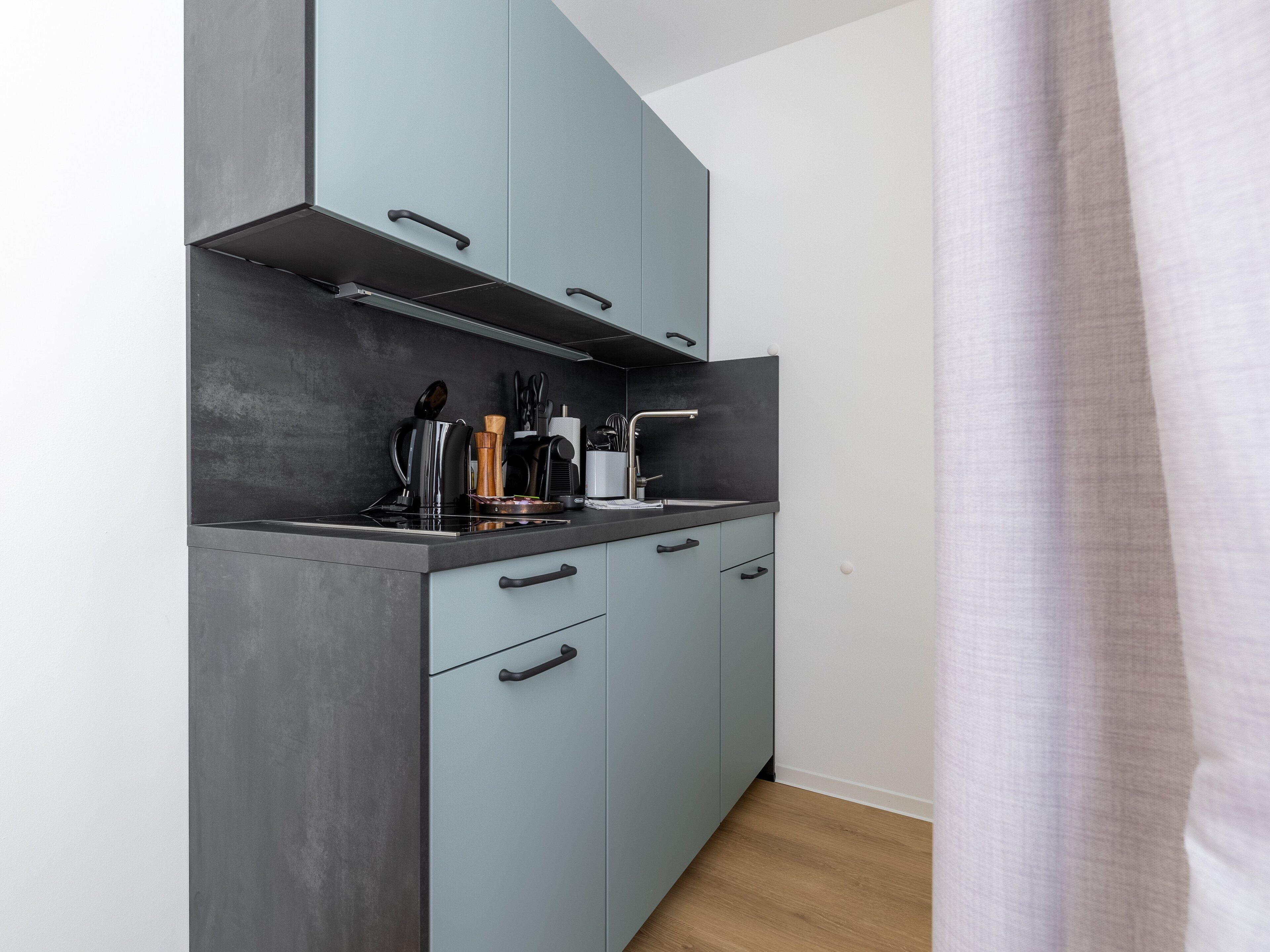 A compact kitchen with grey cabinets, a black countertop, and modern appliances.
