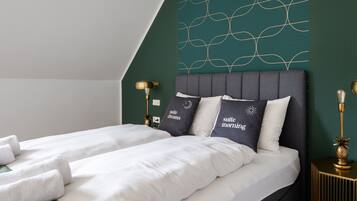 A double bed with white linens, two pillows with text, a gold lamp, and a green accent wall.