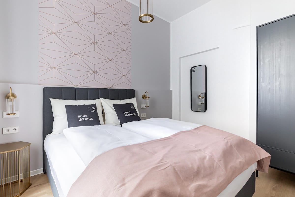 Um quarto moderno com cama, abajures, um padrão geométrico na parede, um espelho e uma porta.