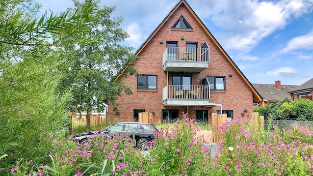 A two-story brick house with a balcony, surrounded by lush greenery and pink flowers. - The Emma vacation apartment in St. Peter-Dorf for up to 4 people (St. Peter-Dorf)