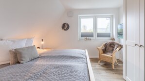 A bedroom with a bed, a chair, a wardrobe, a window, and a wall clock. - The Emma vacation apartment in St. Peter-Dorf for up to 4 people (St. Peter-Dorf)