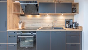 Eine moderne Küche mit grauen Schränken, einem eingebauten Backofen, einer Spüle aus Edelstahl und einer Kaffeemaschine.