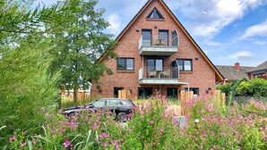 Ein zweistöckiges Backsteinhhaus mit Balkon, umgeben von üppigem Grün und rosa Blüten.