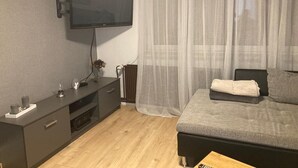 Ein modernes Schlafzimmer mit einem Wand-Fernseher, einem Nachttisch mit Lampe und einem Bett mit grauer Decke.