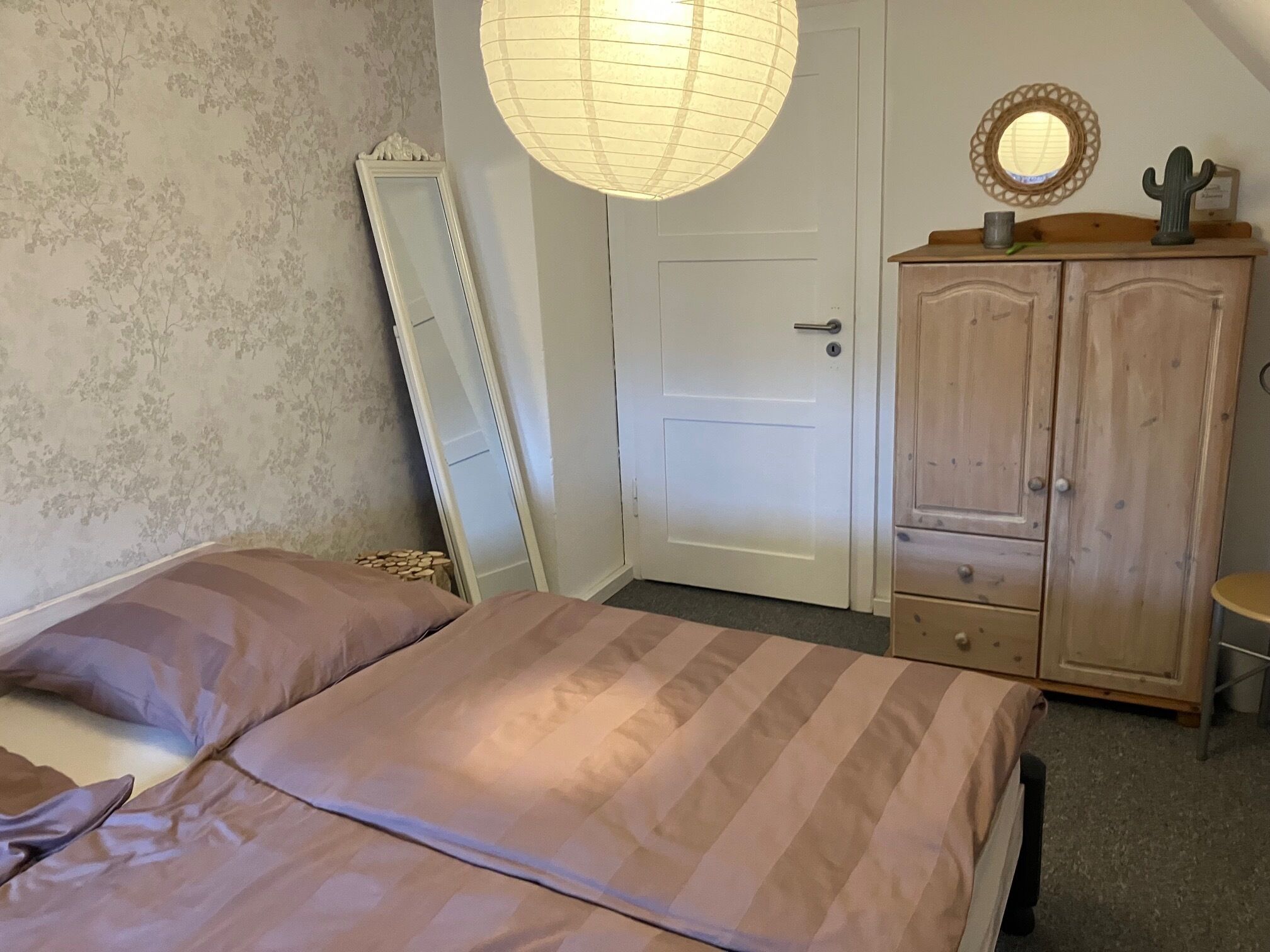 Un dormitorio con cama, armario, espejo y puerta.