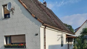 Ein weißes Backsteingebäude mit geneigtem Dach, einer Satellitenschüssel und einem Fenster mit Blumenkasten.