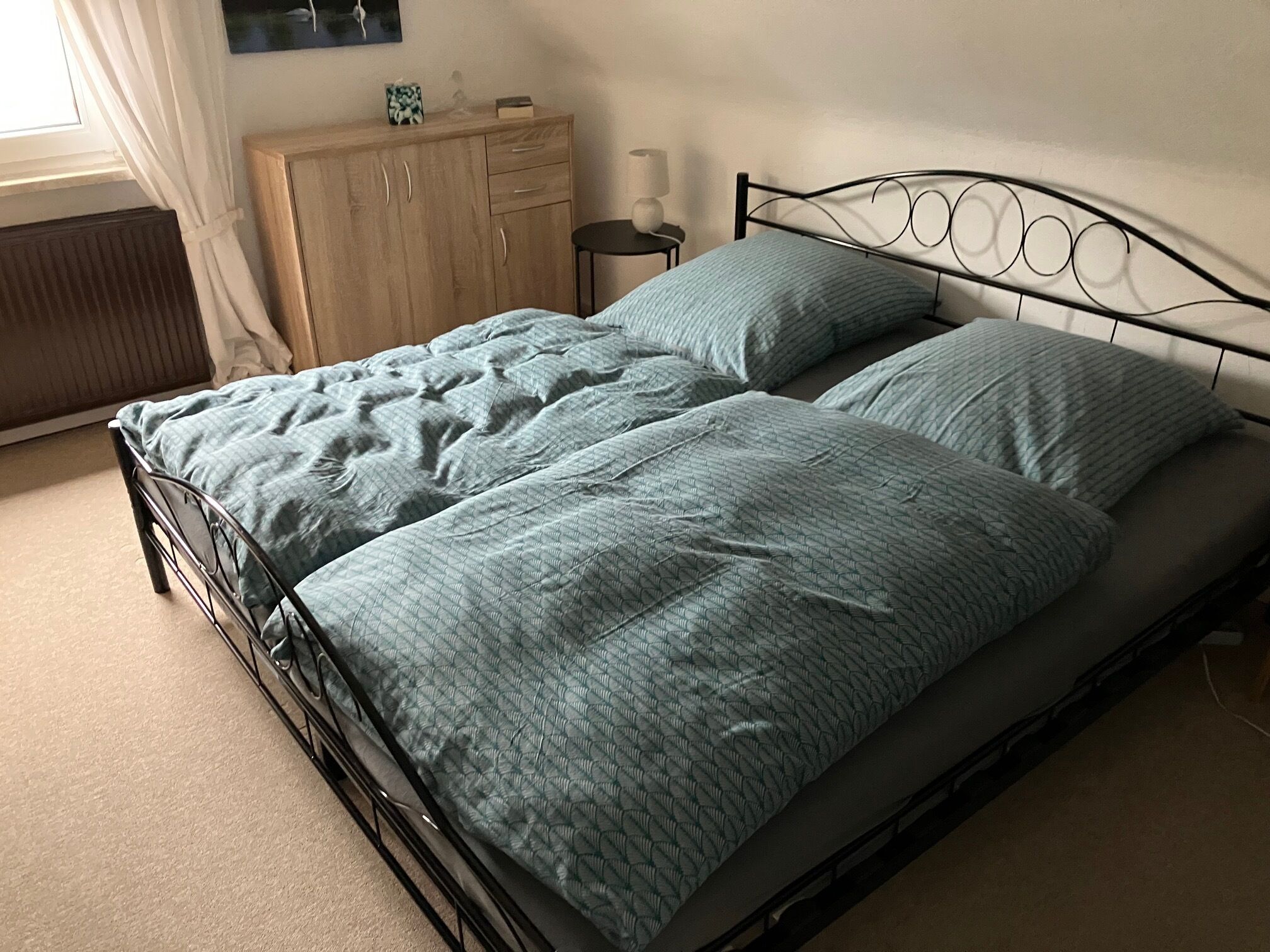 A single bed with a metal frame, a wooden nightstand with a lamp, and a radiator.
