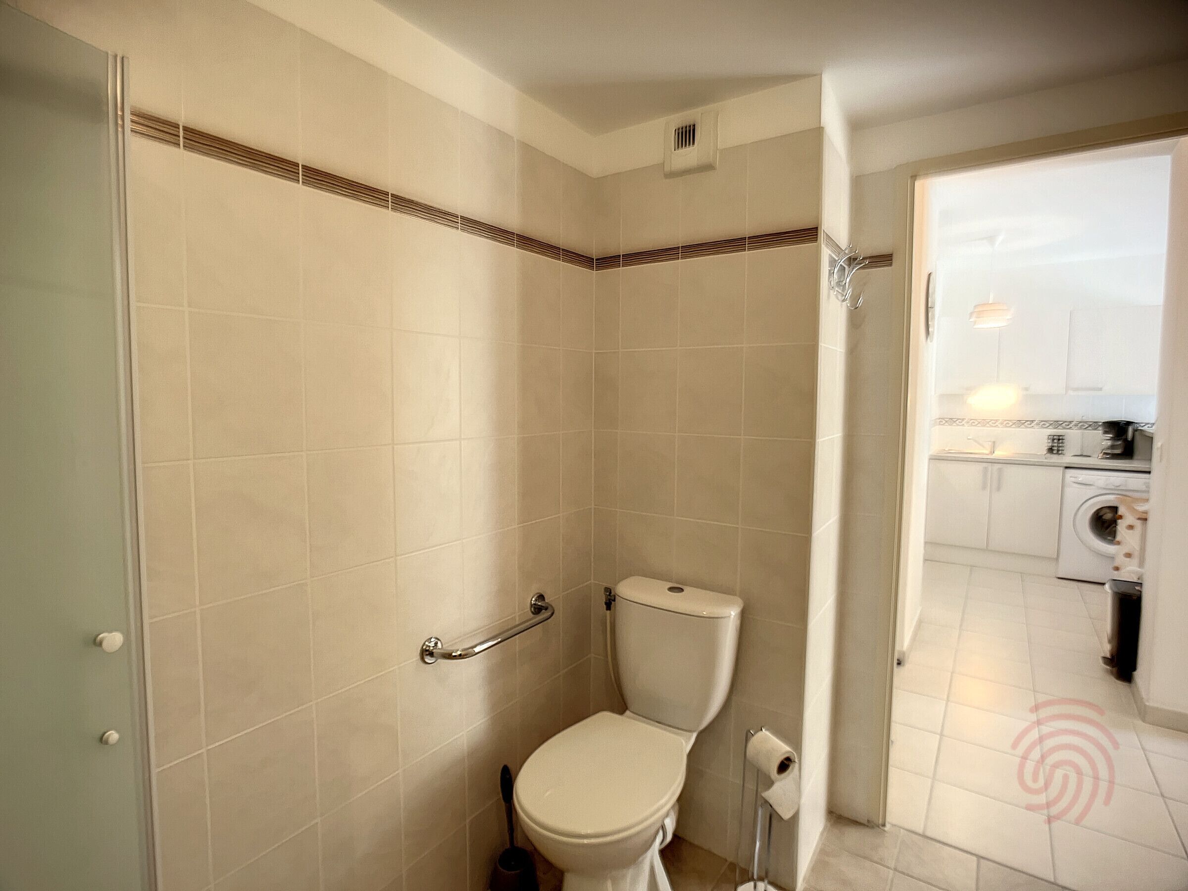 A bathroom with a toilet, a handrail, and a shower area.
