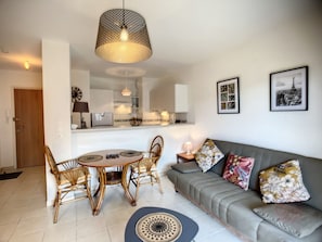 Ein modernes Wohnzimmer mit grauem Sofa, Korbstühlen, einem runden Esstisch und einer Pendelleuchte.