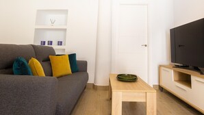 A modern living room with a grey sofa, colorful cushions, a small wooden table, a television, and a white door. - Historic Center Apartment with Modern Comforts & Patio in Estepona (Estepona)
