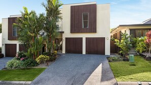 Una casa moderna de dos pisos con entrada de vehículos, garaje y un jardín bien cuidado con diversas plantas y flores.