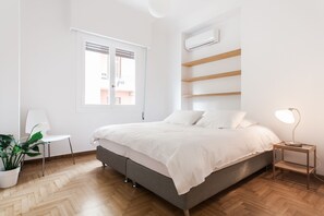 Une chambre à coucher moderne avec un lit, une chaise, une table de chevet, une lampe et une plante en pot.